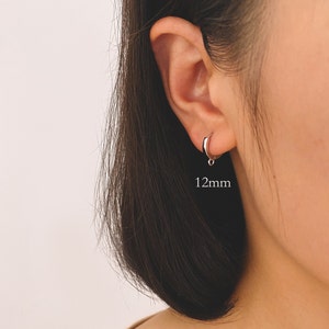 May include: A silver hoop earring with a small dangle charm. The earring is 12mm in diameter.