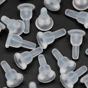 May include: A close-up of a group of clear plastic bottle stoppers. The stoppers have a round base and a narrow neck. They are all arranged in a random pattern on a black surface.