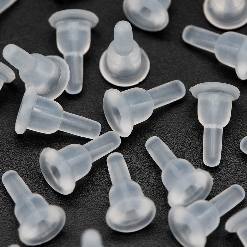 May include: A close-up of a group of clear plastic bottle stoppers. The stoppers have a round base and a narrow neck. They are all arranged in a random pattern on a black surface.