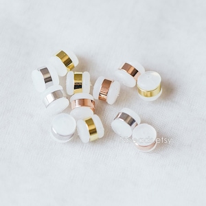 May include: A group of white round beads with gold, silver, and rose gold metal accents. The beads are scattered on a white surface.