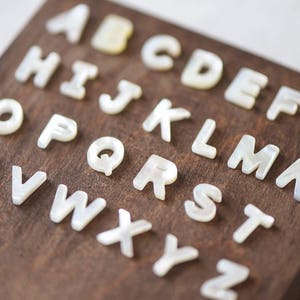 May include: White pearl letter tiles on a dark brown wooden surface, spelling out the alphabet from A to Z.
