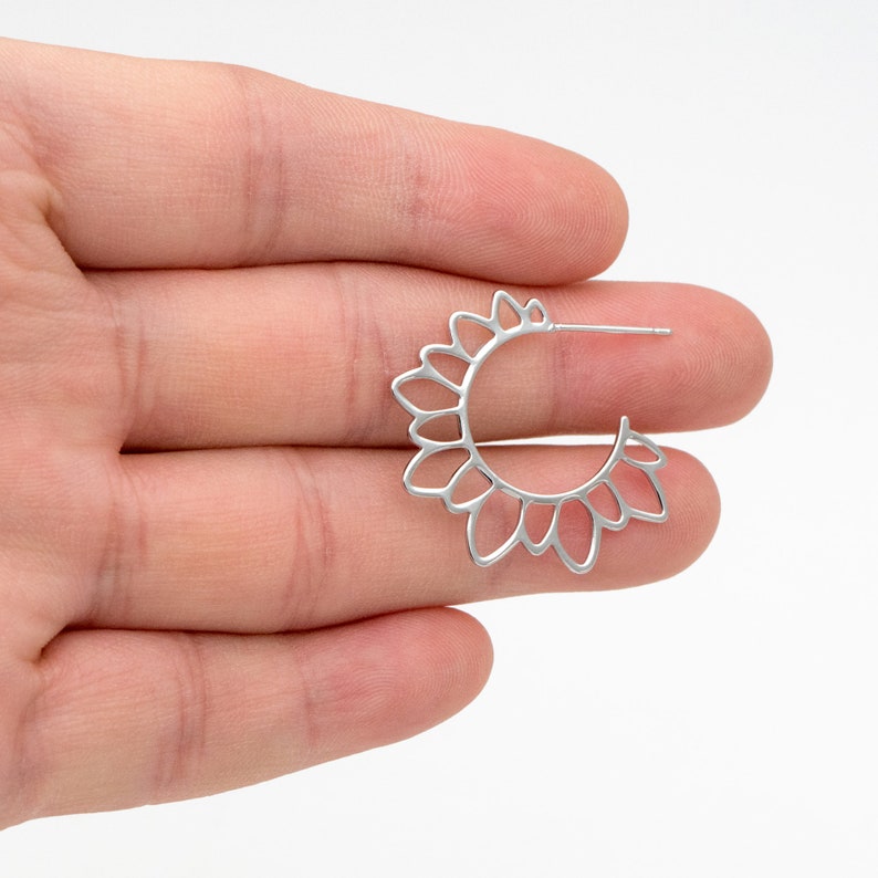 Puede incluir: Pendientes de aro de plata con un delicado dise&ntilde;o floral. Los pendientes est&aacute;n hechos de un metal fino y tienen una forma circular con un patr&oacute;n recortado de peque&ntilde;os p&eacute;talos.