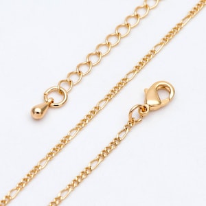 Puede incluir: Un collar de cadena de oro con cierre de mosquetón. La cadena está hecha de dos estilos diferentes, uno con eslabones ovalados y el otro con una cadena plana más delicada.