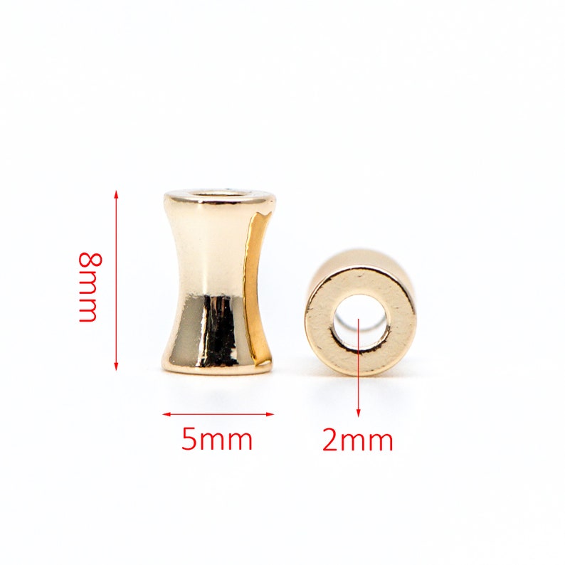 May include: Gold-toned metal bead with a cylindrical shape and a smaller hole in the center. The bead is 8 mm tall, 5 mm wide, and has a 2 mm hole.