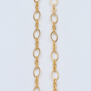 May include: Two gold chains with oval links. The chains are hanging straight down and are parallel to each other.