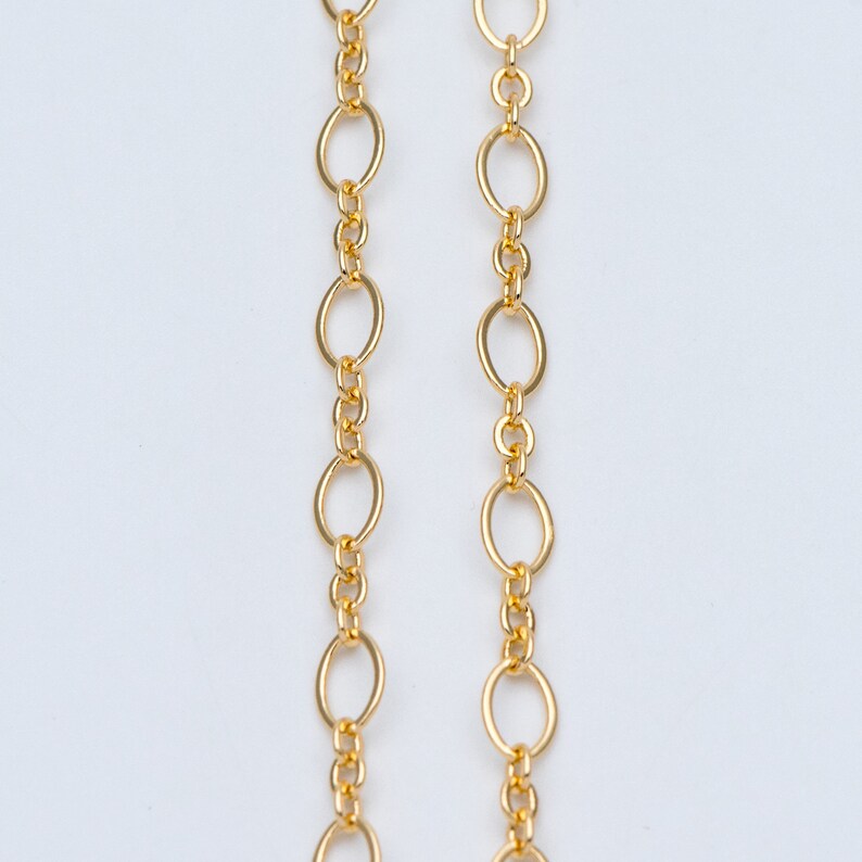 May include: Two gold chains with oval links. The chains are hanging straight down and are parallel to each other.