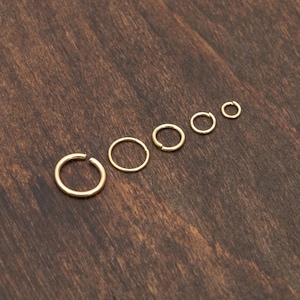 May include: A set of six gold hoop earrings of varying sizes, arranged in order of size from largest to smallest on a wooden surface.