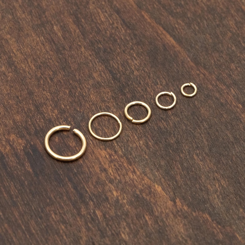May include: A set of six gold hoop earrings of varying sizes, arranged in order of size from largest to smallest on a wooden surface.