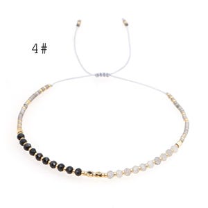 May include: A delicate adjustable bracelet with black and white beads, separated by gold accents. The bracelet is made with a gray cord and has a sliding knot closure.