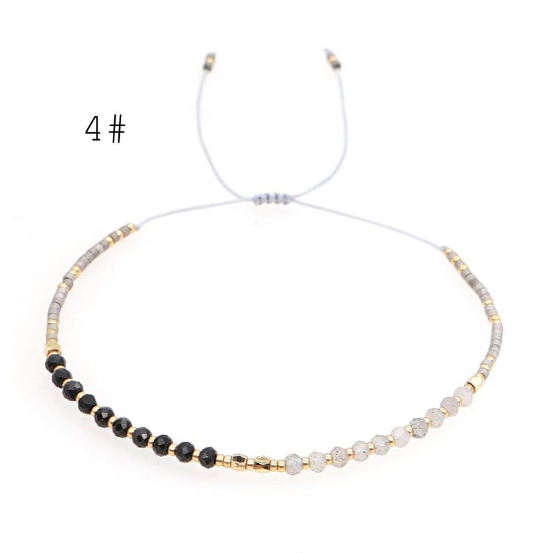 May include: A delicate adjustable bracelet with black and white beads, separated by gold accents. The bracelet is made with a gray cord and has a sliding knot closure.