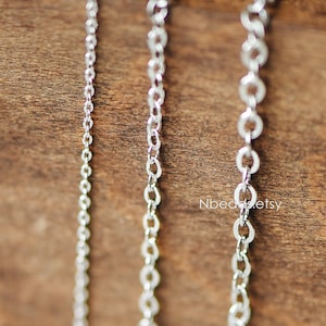 Puede incluir: Tres cadenas plateadas de diferentes grosores, colgando sobre un fondo de madera.