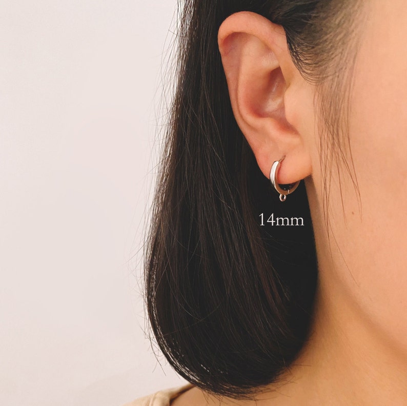 May include: Silver hoop earrings with a small drop charm. The earrings are 14mm in diameter.