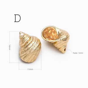 May include: Two gold-colored metal seashell charms labeled D. The left charm measures 14mm by 11mm. The right charm features a visible 1mm hole. Both items have a textured, spiraled surface detail and a metallic finish.