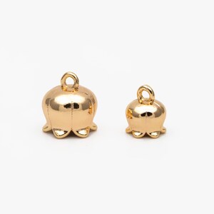 May include: Two gold-colored metal bell charms with a loop at the top for attaching to jewelry or other crafts. The larger charm is about 1.5 inches tall and the smaller charm is about 1 inch tall.