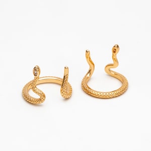 May include: Two gold snake rings with textured details. One ring has a small clear stone on the snake's head.