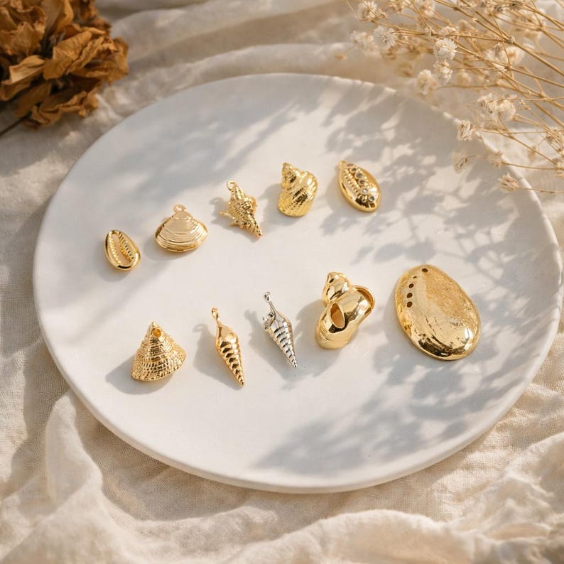 May include: A collection of ten metallic charms shaped like various seashells, including conch, spiral, and clam designs. Nine charms feature a polished gold-tone finish, while one slender spiral charm has a bright silver-tone finish.