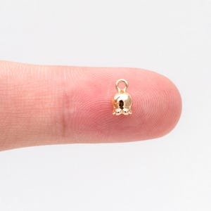 May include: A gold-colored bell charm with a loop at the top. The bell is about the size of a fingernail.