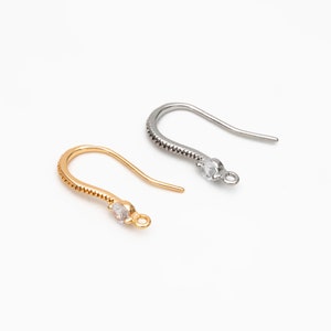 May include: Two earring hooks with a clear rhinestone at the end. One hook is gold and the other is silver.