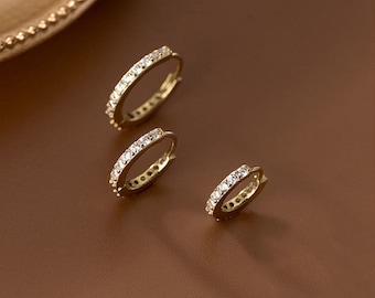 May include: Three gold hoop earrings with a single row of clear cubic zirconia stones.