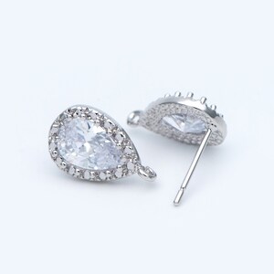 May include: A pair of silver teardrop-shaped earrings with clear cubic zirconia stones. The earrings have a halo setting and a post back.