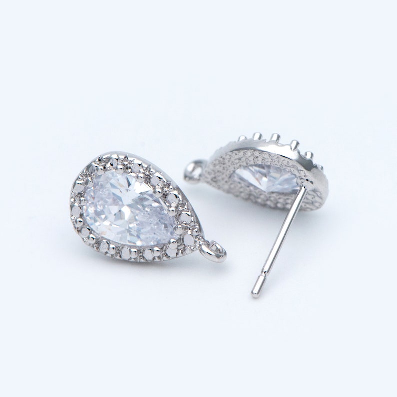 May include: A pair of silver teardrop-shaped earrings with clear cubic zirconia stones. The earrings have a halo setting and a post back.