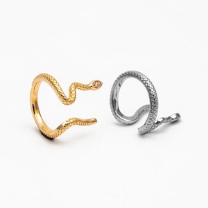May include: Two snake-shaped rings, one gold and one silver. Both rings feature a textured snake design and a small clear stone on the head.