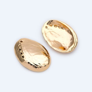 Peut inclure: Deux boucles d'oreilles en forme de coquille d'ormeau dorées avec une finition lisse et brillante. Chaque coquille a cinq petits trous autour du bord.