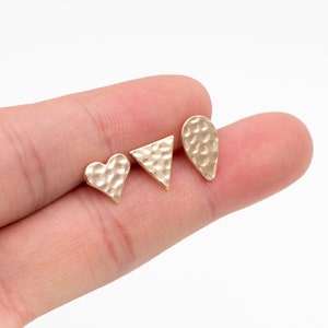 May include: Three gold-toned earrings with hammered textures. The earrings are shaped like a heart, a triangle, and a teardrop.