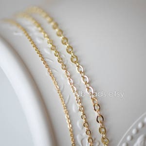 May include: Three gold chains of different thicknesses and lengths are displayed on a white surface. The chains are made of a delicate, linked design.