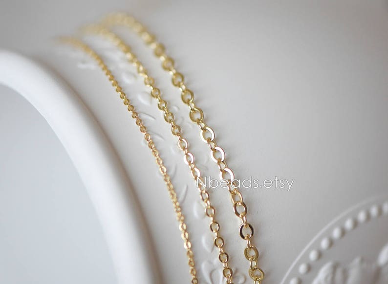 May include: Three gold chains of different thicknesses and lengths are displayed on a white surface. The chains are made of a delicate, linked design.