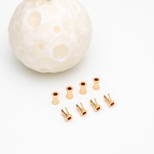 May include: Eight gold-colored metal bead caps with a smooth, rounded finish. The caps have a small hole in the center and are designed to be used as end caps for jewelry making.