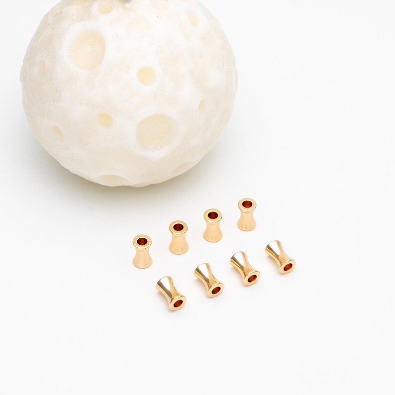 May include: Eight gold-colored metal bead caps with a smooth, rounded finish. The caps have a small hole in the center and are designed to be used as end caps for jewelry making.