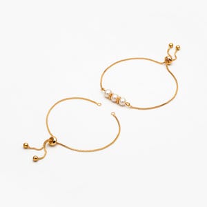 Puede incluir: Dos pulseras de cadena dorada con nudos deslizantes ajustables. Una pulsera tiene tres cuentas de perlas blancas.