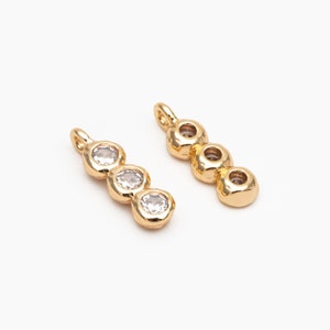 Peut inclure: Deux breloques pendantes dorées, chacune avec trois pierres rondes transparentes. Les breloques sont conçues pour la fabrication de bijoux.