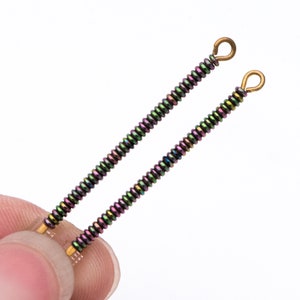 Puede incluir: Dos hebras de cuentas iridiscentes con bucles de metal dorado en los extremos. Las cuentas son una mezcla de verde, morado y negro.