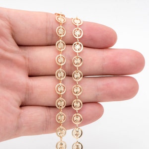 Op de afbeelding: Een gouden ketting met een delicaat, gepatroneerd ontwerp. De ketting is gemaakt van kleine, ronde schakels met een bloemmotief.