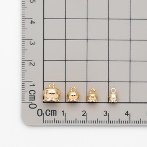 May include: Four gold-colored bell charms of varying sizes, measured in centimeters on a ruler.