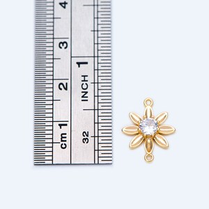 May include: Gold-tone flower charm with a clear rhinestone center. The charm is about 1 inch in diameter and has a loop on the top for attaching to jewelry.
