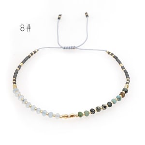 May include: A delicate adjustable bracelet with a mix of light blue, green, and gray beads. The bracelet is made with a gray cord and gold accents.