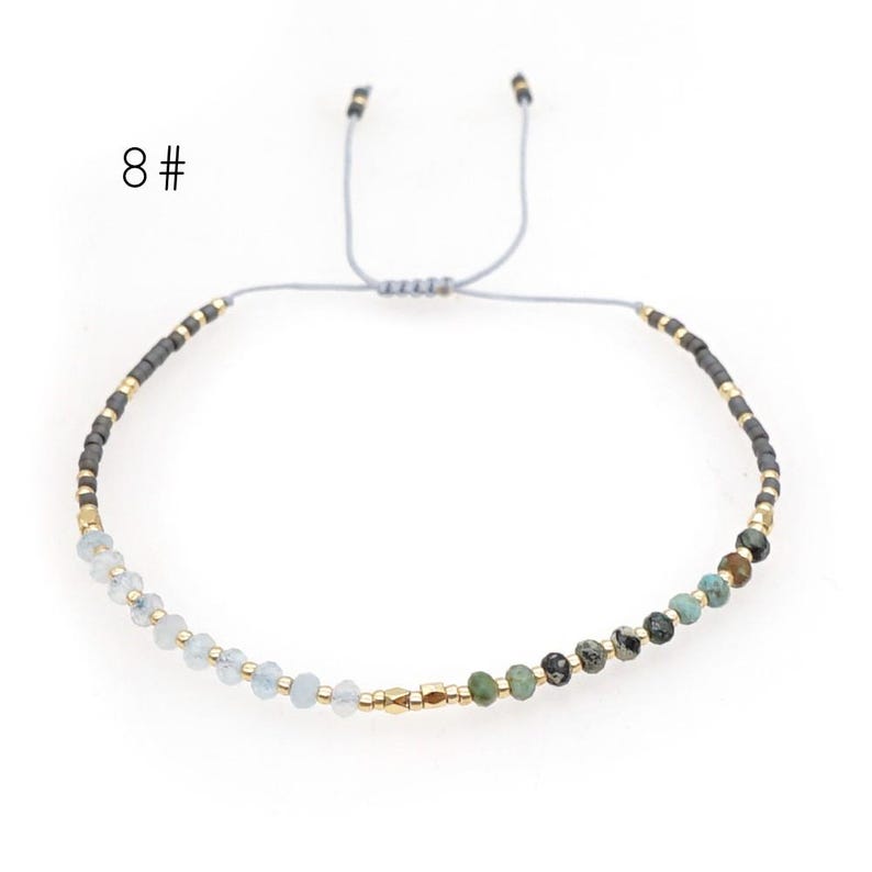 May include: A delicate adjustable bracelet with a mix of light blue, green, and gray beads. The bracelet is made with a gray cord and gold accents.