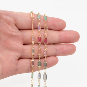 May include: Three gold chains with rectangular, faceted gemstones. The chains feature different colored gemstones: pink, light green, and blue.