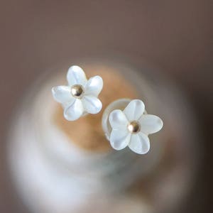 K&ouml;nnte beinhalten: Ein Paar wei&szlig;e, blumenf&ouml;rmige Ohrringe mit goldenen Zentren. Die Ohrringe sind klein und zart.