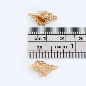May include: Two gold-colored seashell charms, each measuring approximately 1 inch in length. The charms are detailed with intricate ridges and a hole for attaching to jewelry.