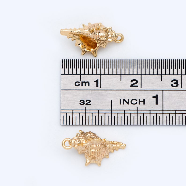 May include: Two gold-colored seashell charms, each measuring approximately 1 inch in length. The charms are detailed with intricate ridges and a hole for attaching to jewelry.