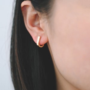 Op de afbeelding: Een paar gouden creolen met een vierkante vorm. De oorbellen worden in de oorlel gedragen.