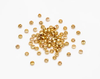 May include: A large pile of gold-coloured metal jump rings, scattered on a white surface. The rings are small and round, with a smooth finish.