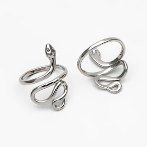 May include: Two silver snake rings. The rings are coiled in a snake-like design, with the head of the snake raised on one ring. The rings are on a white background. Jewellery.