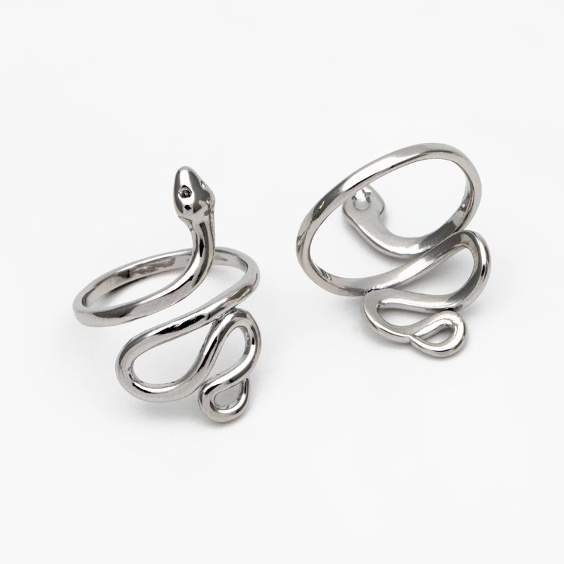 May include: Two silver snake rings. The rings are coiled in a snake-like design, with the head of the snake raised on one ring. The rings are on a white background. Jewellery.