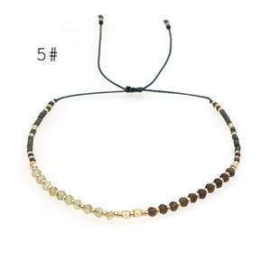 May include: A delicate adjustable bracelet with a black cord and a mix of green and brown beads. The bracelet has a simple design and is perfect for everyday wear.