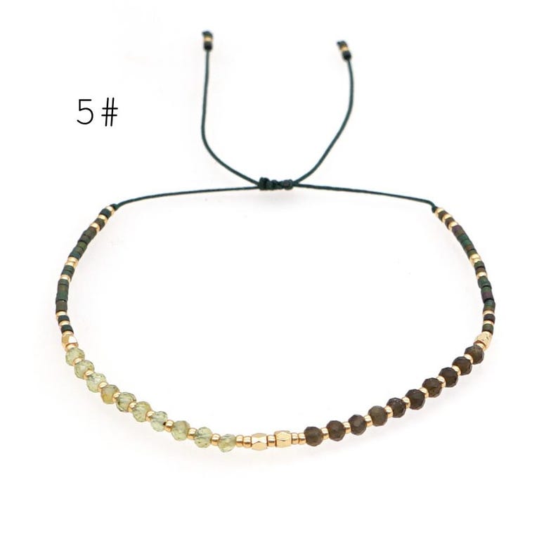 May include: A delicate adjustable bracelet with a black cord and a mix of green and brown beads. The bracelet has a simple design and is perfect for everyday wear.